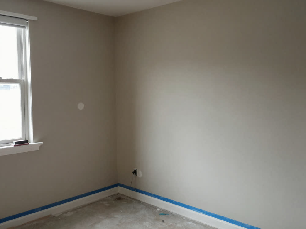 Bedroom with patched walls and blue-taped baseboards prepped for painting