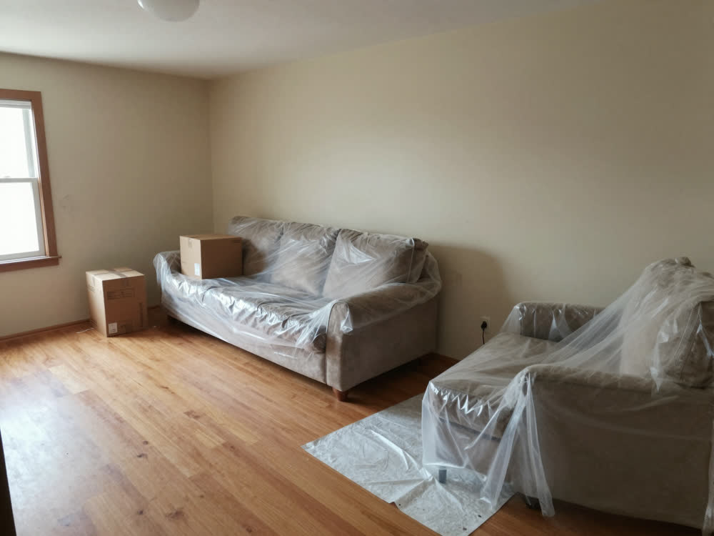 Living room with furniture covered in plastic sheeting, prepped for a full repaint